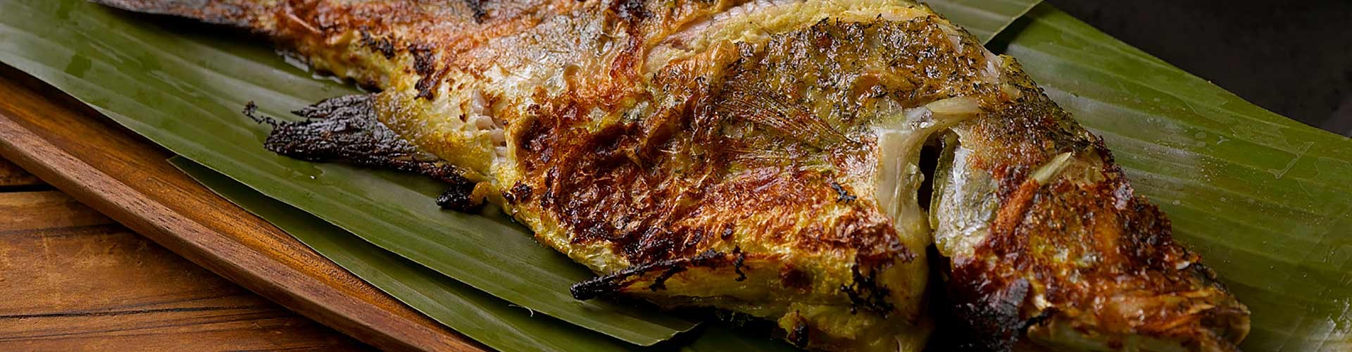 Grilled fish served on a banana leaf, showcasing a crispy skin and flavorful spices.