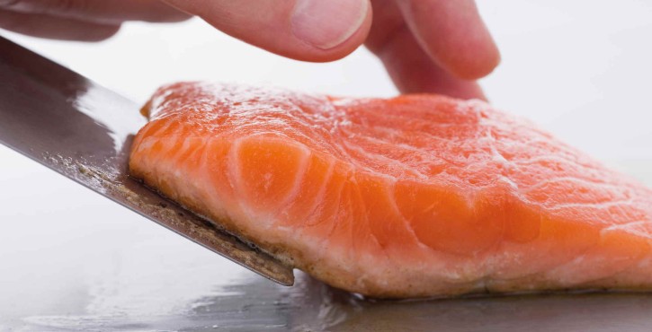 A hand gently touching a fresh salmon fillet on a stainless steel surface with a knife beside it.