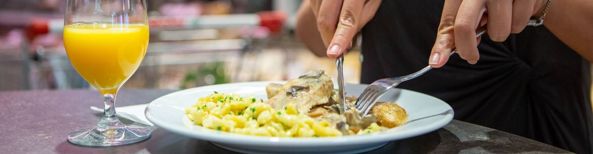 Une personne dégustant un plat de pâtes et de poulet, avec un verre de jus d‘orange à proximité, dans un restaurant décontracté.