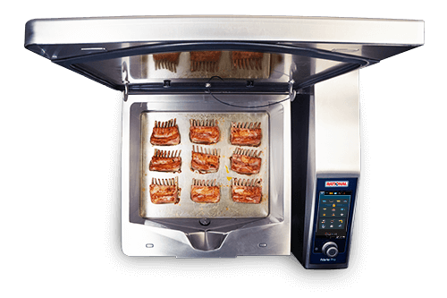 El Rational iVario Pro L con la tapa abierta, mostrando costillas de cordero a la parrilla sobre la superficie de cocción.