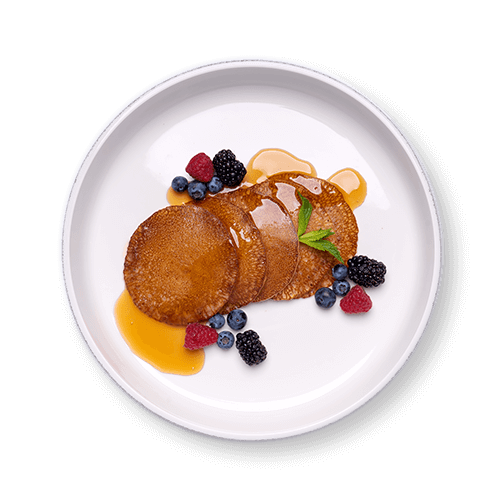 A plate of fluffy pancakes drizzled with syrup, garnished with fresh berries and a sprig of mint.