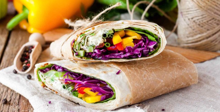 Un gros plan sur un burrito aux légumes, rempli de légumes colorés comme de la salade, du chou rouge et des poivrons, sur une table rustique.