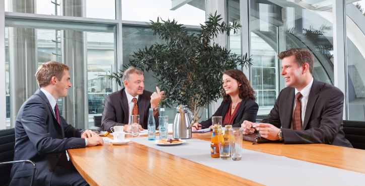  Four people in suits having a discussion in a modern conference room.