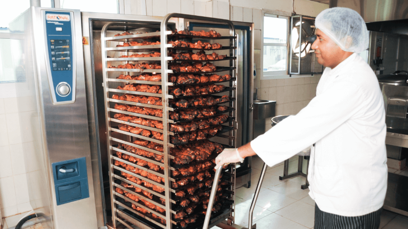 Chef loading skewered meat into a Rational oven with multiple racks.