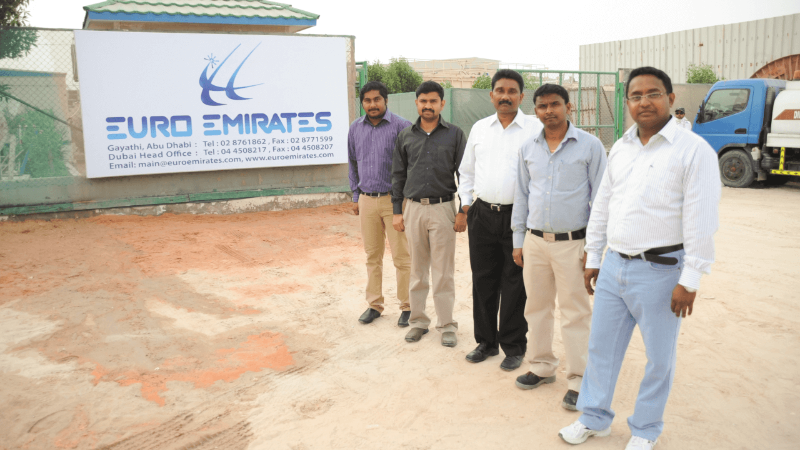 Group of men standing in front of the Euro Emirates sign at a business location.
