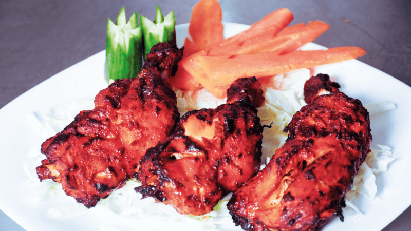 Grilled chicken pieces served on a plate with lettuce, carrots, and cucumber garnish.