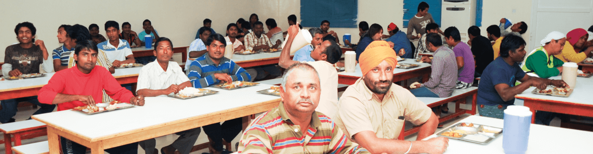 Group of men dining together in a cafeteria, enjoying their meals on trays.