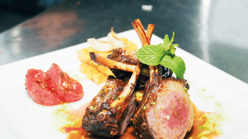 Plate of roasted lamb chops with sauce, tomatoes, and mint garnish.
