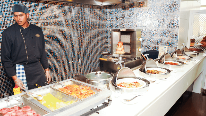 Chef standing by a buffet with various dishes and a shawarma grill.