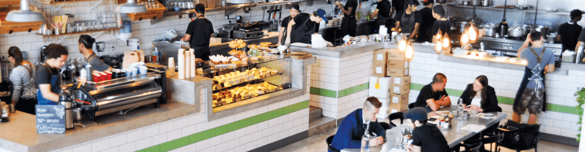 A busy bakery cafe with several employees working behind the counter and customers seated at tables.