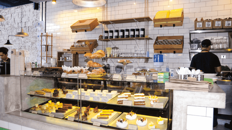 A bakery display filled with various pastries and desserts, with an employee working behind the counter.