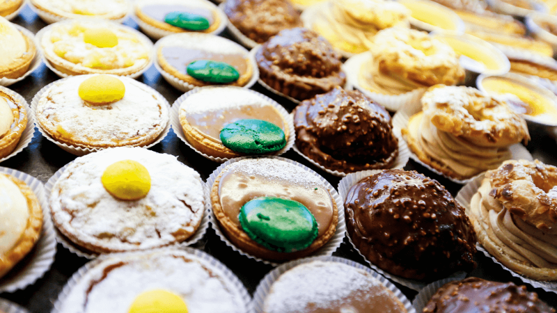 A variety of colorful pastries displayed on a tray, featuring lemon and chocolate flavors, some topped with vibrant green and yellow decorations.