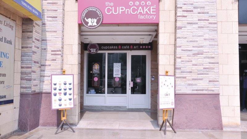 Exterior view of the Cupcake Factory shop with signage and displays featuring various cupcakes.