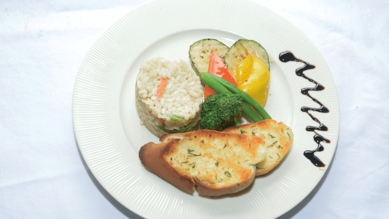 A plate of food with rice, grilled vegetables, and garlic bread, drizzled with balsamic sauce.
