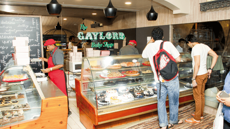 The interior of Gaylord Bake Shop with a display of cakes and pastries, and people browsing the display.