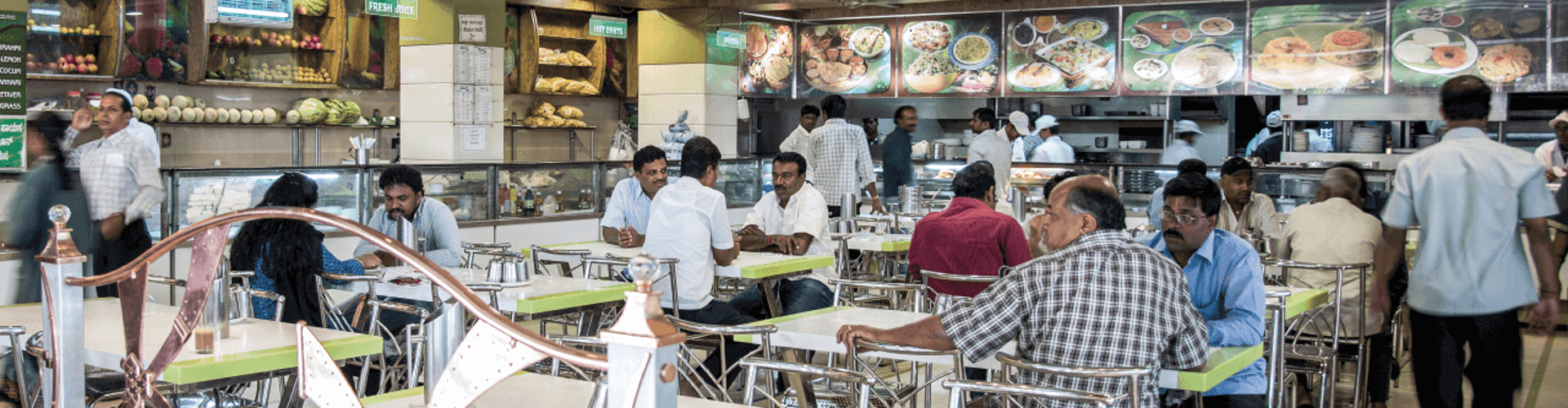 A busy restaurant with people sitting at tables, and staff working behind the counter with food displayed on the menu boards.