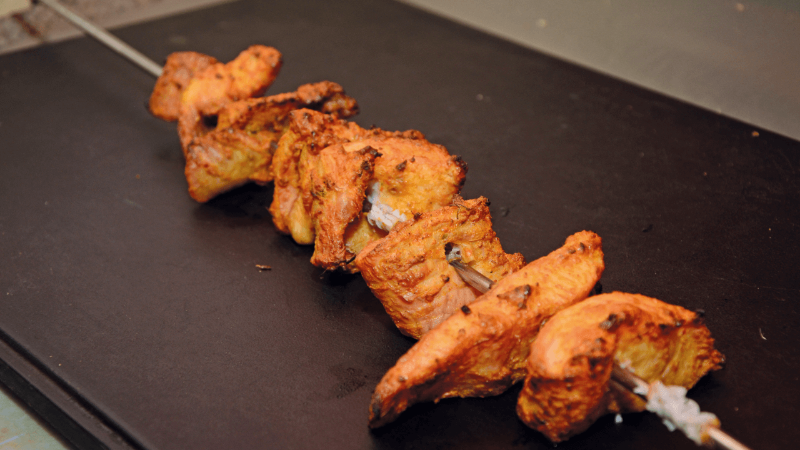 Close-up of grilled chicken pieces on a skewer, resting on a grill tray.