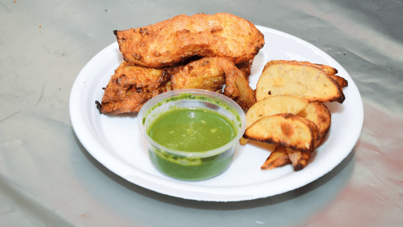 A plate with grilled chicken pieces, fried potato slices, and a side of green chutney.