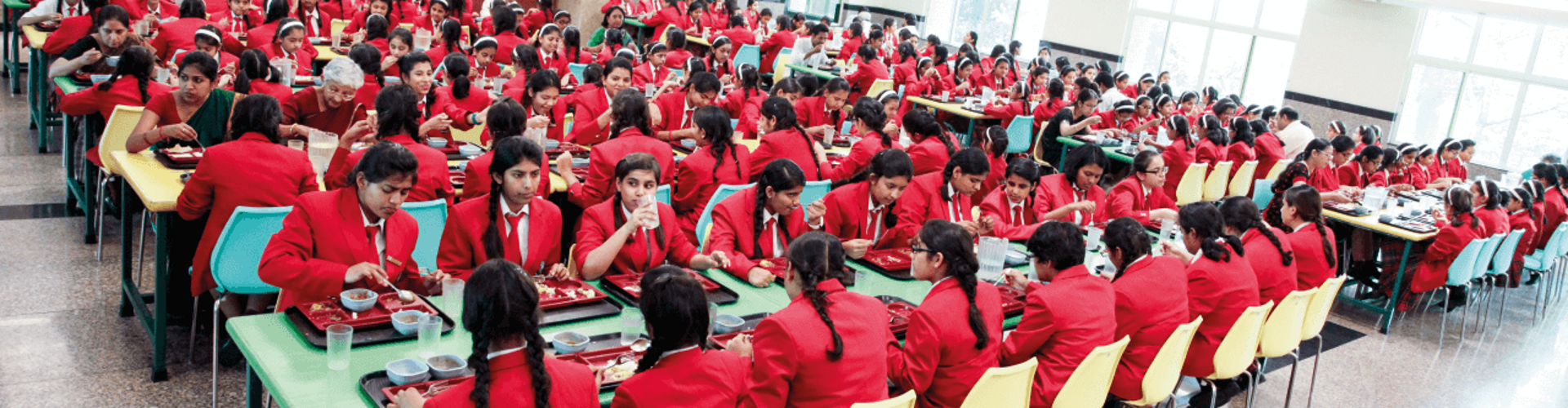 Students in red uniforms seated at tables in a busy school cafeteria.