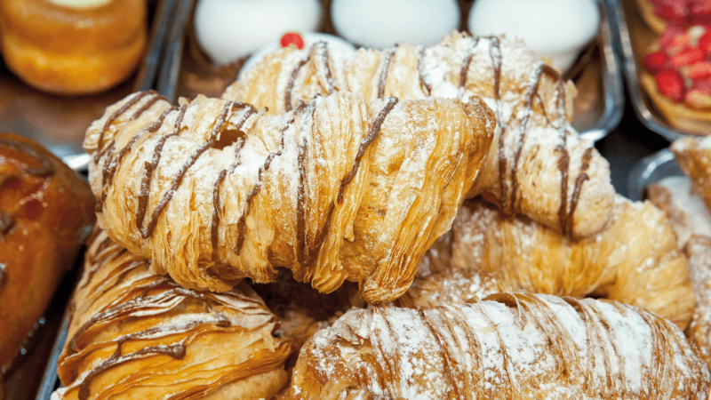 Close-up of assorted pastries, including chocolate-drizzled croissants and sweet doughnuts with frosting.