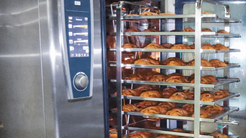 Close-up of a Rational oven with racks filled with freshly baked pastries.