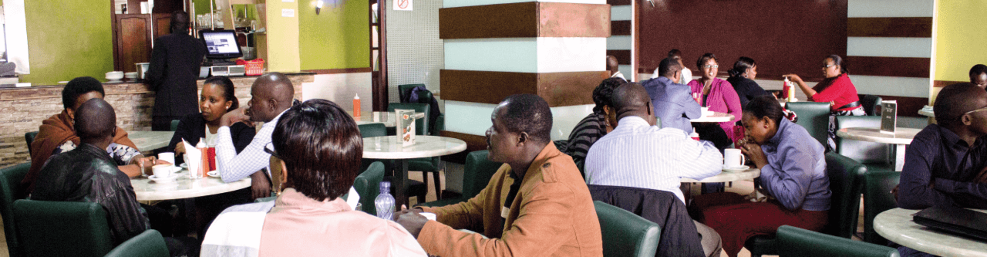 A busy cafe with people sitting at tables, talking and enjoying their drinks, surrounded by colorful decor
