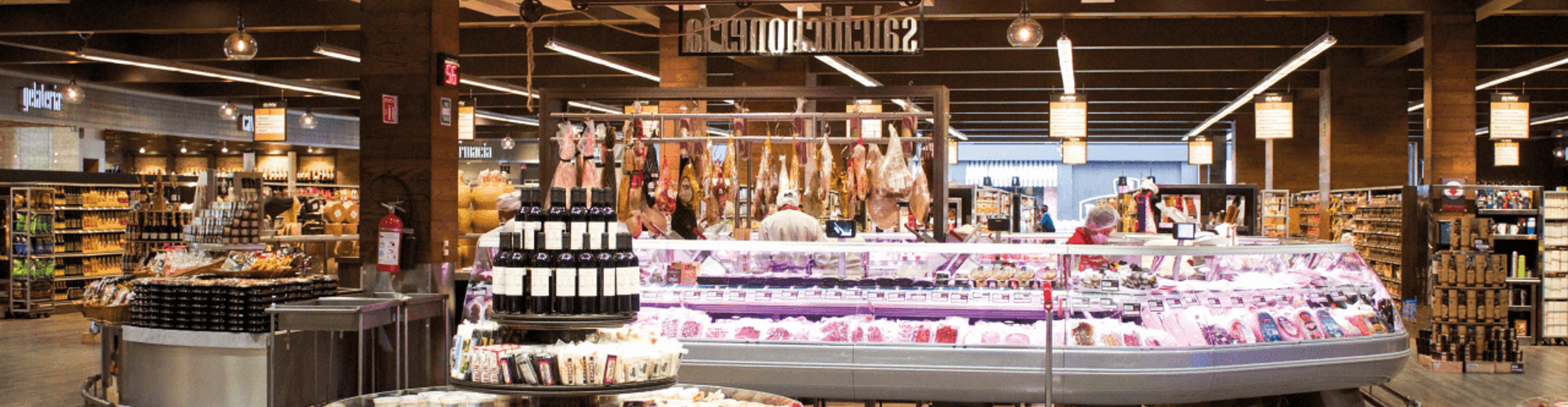 The interior of a modern grocery store with a display of meats, dairy, and a well-lit shopping area.