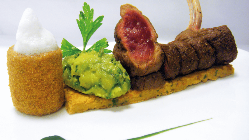 Ein Gourmetgericht mit Filetsteak, püriertem Avocado, einer knusprigen Kroketten und grüner Sauce, garniert mit Petersilie.