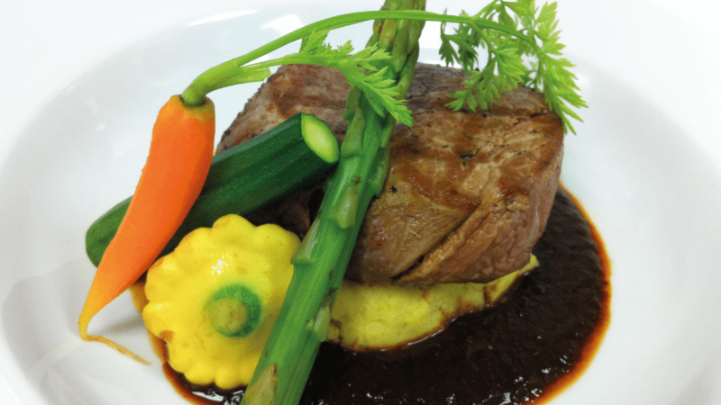 Ein Teller mit zartem Steak, Kartoffelpüree, geröstetem Gemüse und einer kräftigen braunen Sauce.