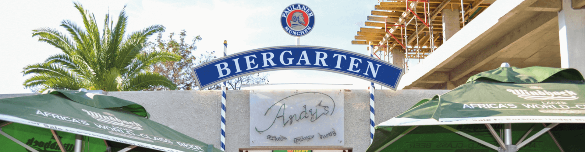 A Biergarten entrance with a sign reading "Biergarten," outdoor tables with green umbrellas, and a couple sitting at a table.