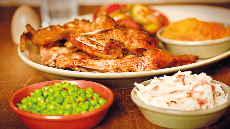 Platter of grilled chicken served with sides of coleslaw, green peas, and a mix of fresh vegetables.