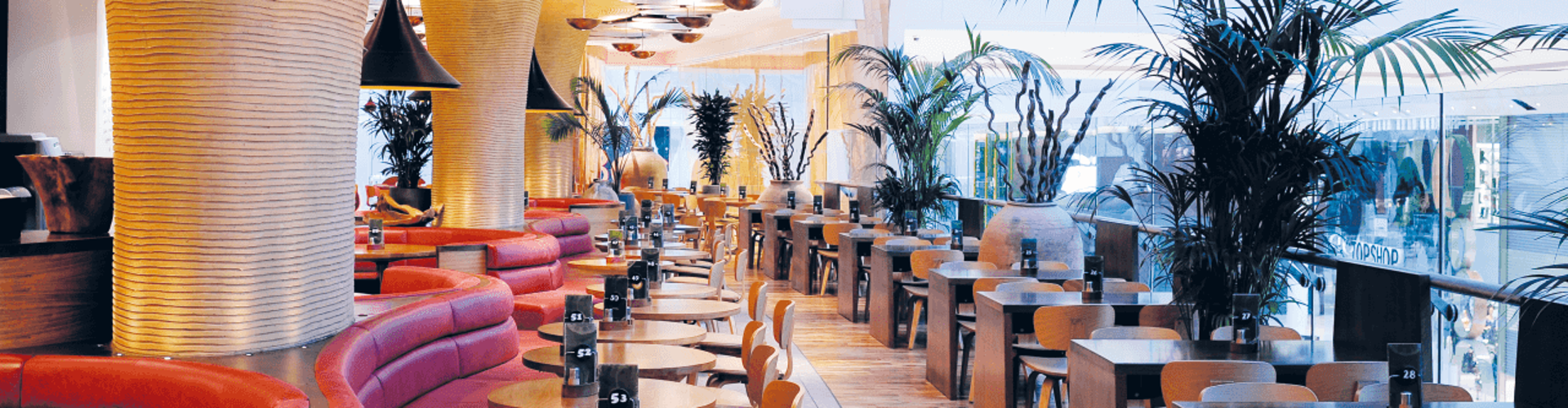 Interior view of a modern restaurant featuring unique architectural columns, wooden tables, and lush greenery.