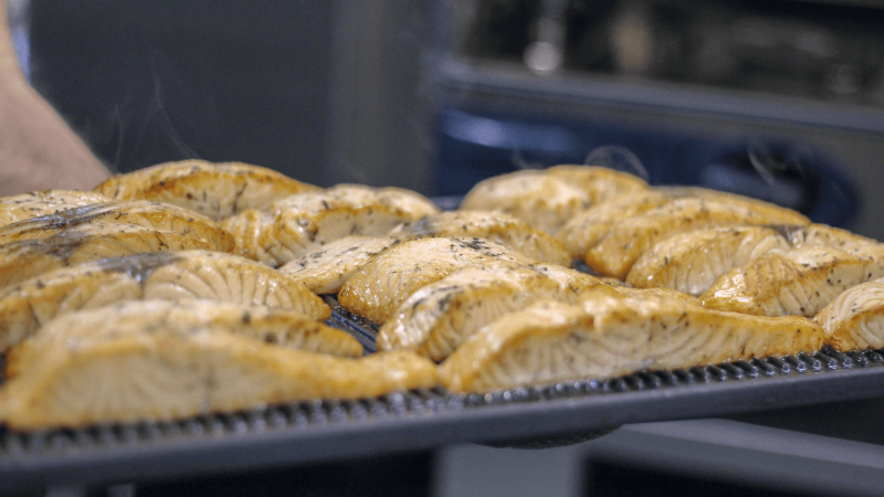 Close-up of perfectly grilled salmon fillets on a baking tray, emitting steam, highlighting their juicy texture.
