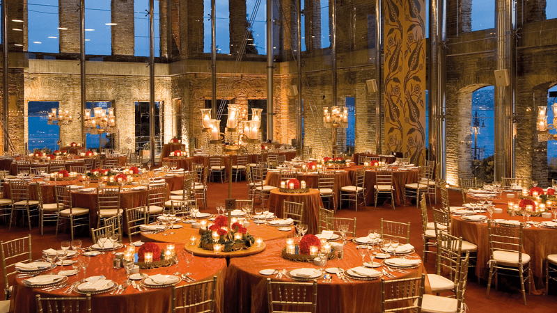 Elegant dining setup in a restaurant with large tables, candles, and a view of the city through glass windows.