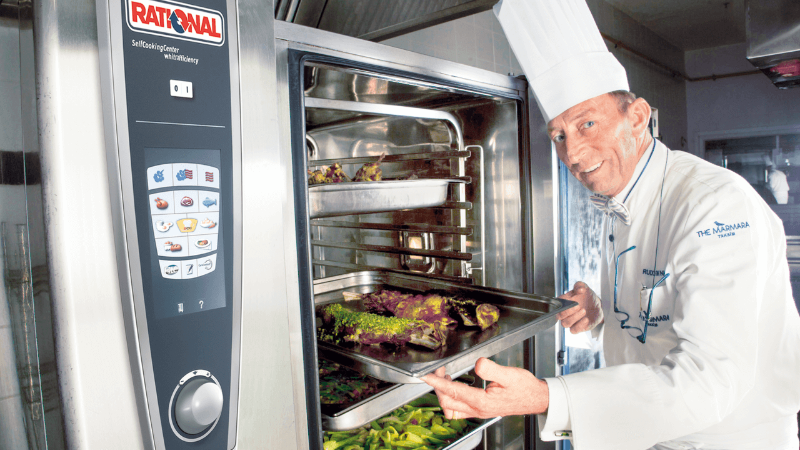 A chef presenting trays of vegetables from a RATIONAL cooking system in a kitchen.