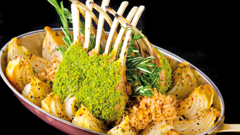A dish with crusted rack of lamb, roasted onions, rice, and fresh rosemary.