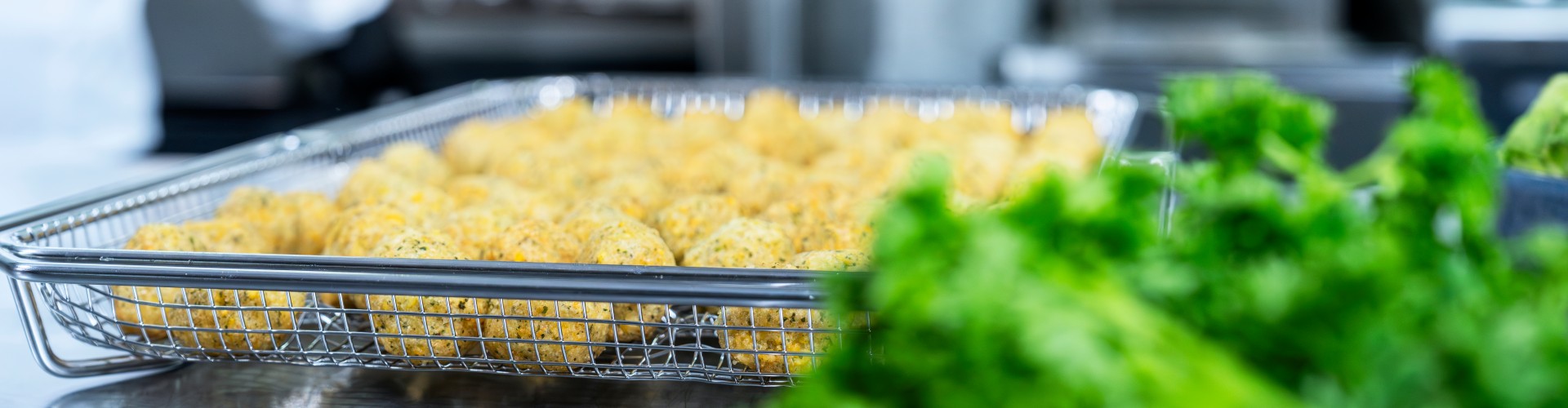 Teglia con polpette di verdure davanti al RATIONAL iCombi Pro forno professionale, erbe fresche in primo piano.