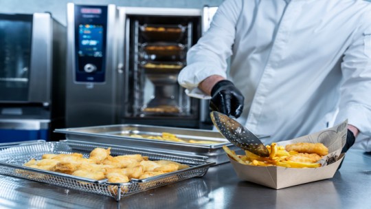 Chef che impiatta fish and chips accanto al RATIONAL iCombi Pro forno professionale.