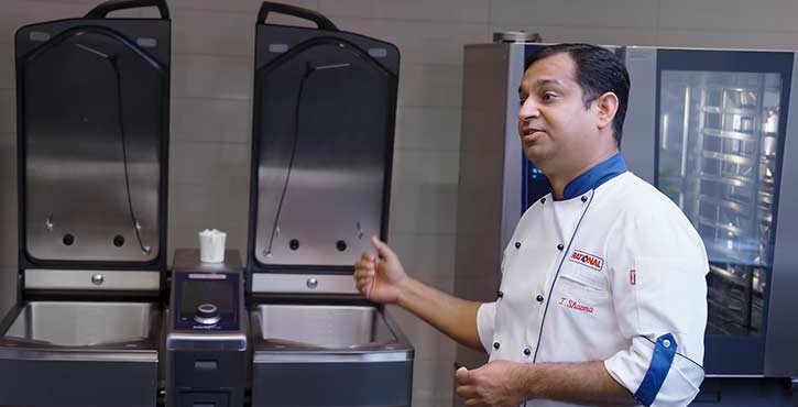 A chef in a white uniform presenting a Rational iVario Pro and iCombi Pro, explaining their features and functionality.