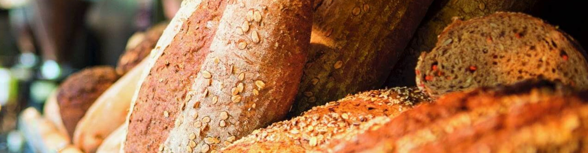 Freshly baked bread on display in a bakery with a woman in the background preparing something.