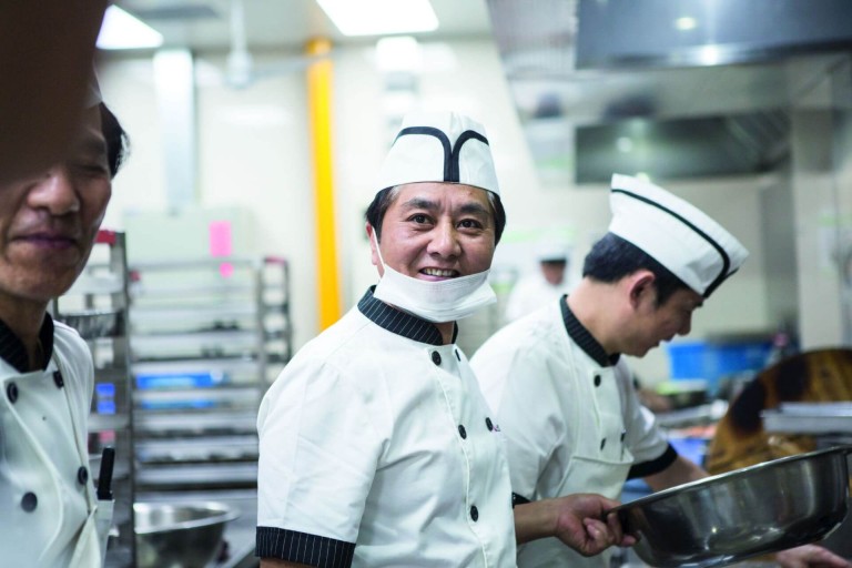 Tres chefs en una cocina de restaurante, uno sonríe a la cámara.