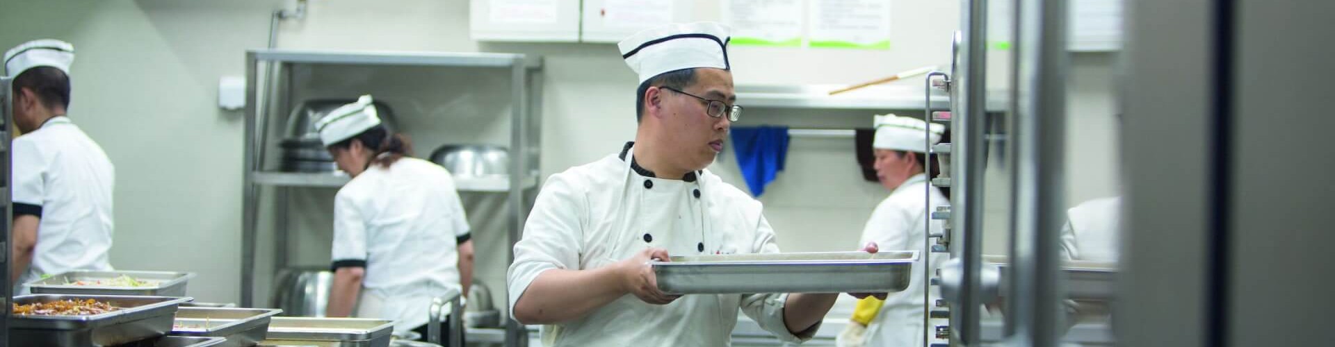 Chef holding tray in front of RATIONAL iCombi Pro combi oven in busy kitchen.
