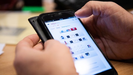 En person holder en smarttelefon og navigerer gjennom en app for data- og programadministrasjon.