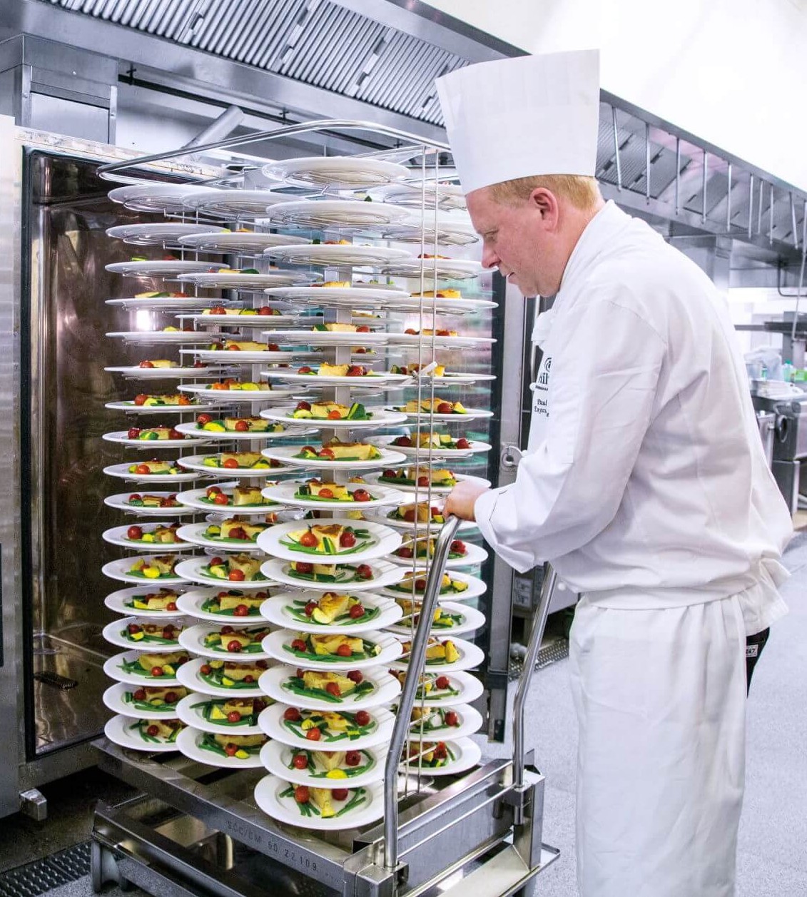 A chef carefully arranging a stack of beautifully plated dishes in a kitchen, demonstrating culinary artistry and attention to detail.