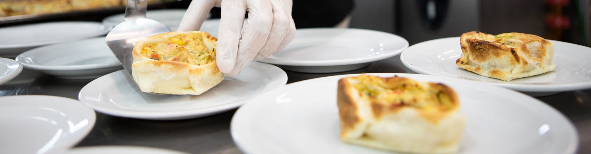 Chef servindo porções individuais de quiche de legumes em uma cozinha profissional.