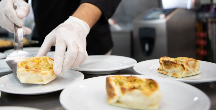 Chef plating a vegetable-filled pastry on a white plate in a busy kitchen.