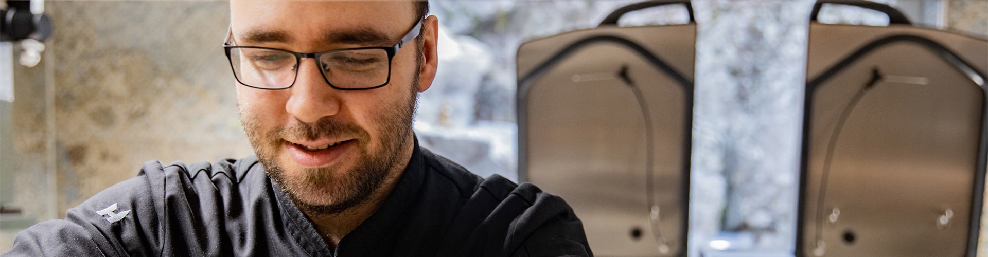 Chef sorridente che lavora in cucina con unità di cottura sullo sfondo.