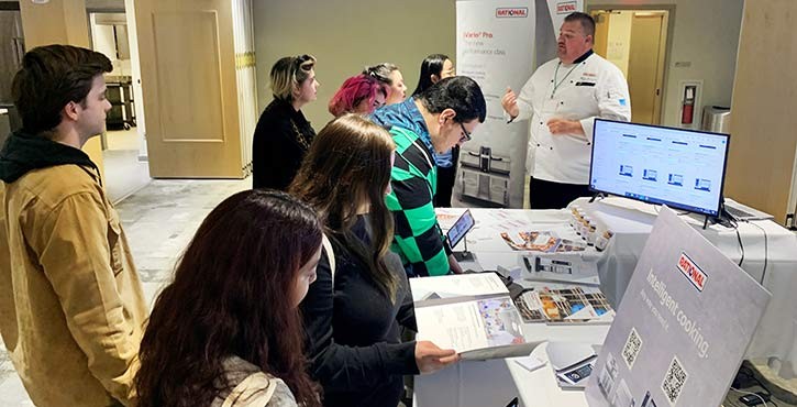 A chef presenting cooking demonstrations to a group of attendees at a Rational display.