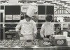 A black-and-white photo of two individuals at a Rational booth during a trade show, one in a chef‘s uniform and hat, preparing food.