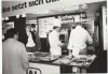 A black-and-white photo of a Rational trade show booth with chefs demonstrating cooking to an audience, featuring various dishes on display.